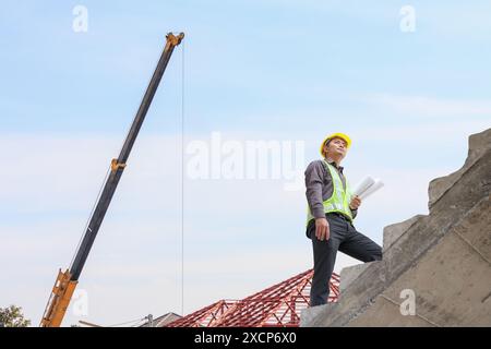 homme d'affaires ingénieur ouvrier dans le casque de protection et le papier de plans à portée de main sur le chantier de construction Banque D'Images