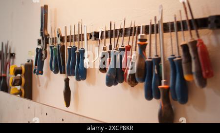 Ciseaux, tournevis, clé et pinces sur le mur dans l'atelier d'assemblage de meubles, plan panoramique. Gros plan de divers outils de travail du bois sur rack dans la menuiserie utilisée pour travailler avec des matériaux en bois Banque D'Images