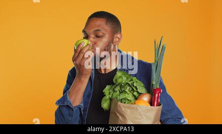 Mec végétalien afro-américain prenant une bouchée d'une pomme verte naturelle mûre, mangeant des fruits biologiques fraîchement récoltés en studio. Personne faisant la publicité de l'agriculture locale et des produits d'origine éthique. Caméra A. Banque D'Images