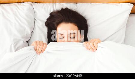 Femme brune se cachant sous couverture dans le lit Banque D'Images