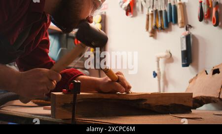 Artisan utilisant un étau d'établi pour tenir le bloc de bois, sculptant des motifs complexes dans le bois à l'aide d'un burin et d'un marteau. L'artiste utilise l'outil d'étau pour serrer le morceau de bois, façonner la bûche avec des outils, caméra B gros plan Banque D'Images