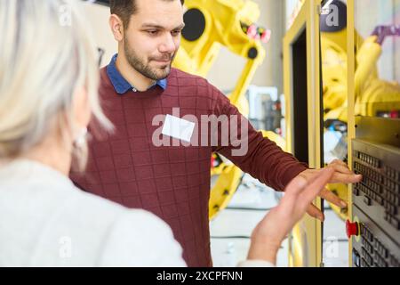 Ingénieurs collaborant à la programmation d'un bras robotique pour l'automatisation des processus. Ils sont dans une usine de fabrication de haute technologie. Banque D'Images