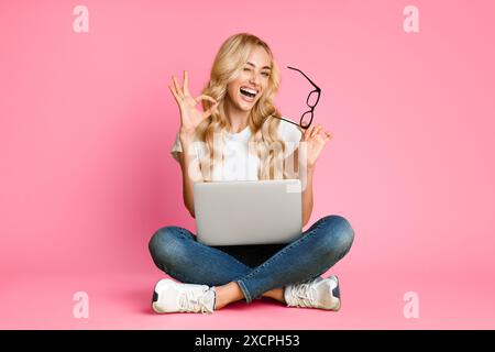 Heureuse jeune femme assise Cross-Legged avec ordinateur portable et lunettes Banque D'Images