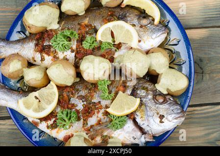 Poisson dorado cuit au four et jeunes pommes de terre dans une assiette avec assaisonnement à la gremolata et sauce à la crème, garni de quartiers de citron vert et de persil en tas. Cuisine à domicile. Banque D'Images