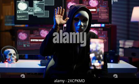 Pirate informatique dissimulant une identité filmant une vidéo de rançon dans une base souterraine cachée, menaçant de divulguer publiquement des données volées si les demandes de paiement ne sont pas satisfaites, utilisant le téléphone pour enregistrer des images de chantage, caméra A. Banque D'Images