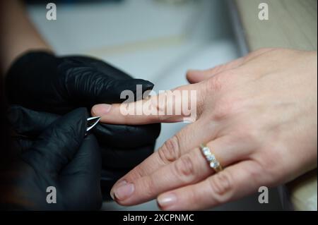 Gros plan d'un processus de manucure dans un salon de beauté. Mains gantées fournissant des services de soins des ongles à un client. Banque D'Images