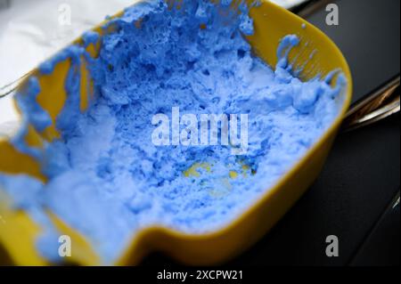 Image en gros plan du mélange bleu de teinture capillaire dans un récipient jaune dans un salon de beauté, prêt pour la coloration des cheveux. Banque D'Images