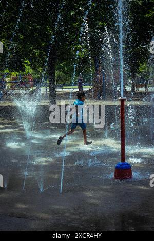 Un enfant qui court à travers le jet d'eau au parc des fontaines de jeu Banque D'Images