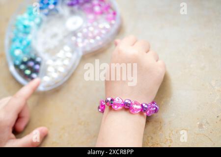 Mains de fille avec bracelet close-up, activités d'art et d'artisanat, projet d'artisanat de bricolage, fabrication de bracelet personnalisé avec des perles colorées, motricité fine Banque D'Images