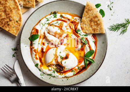 Œufs turcs Cilbir et pain pita frais pour le petit-déjeuner turc traditionnel. Plat de mezze turc. Oeufs pochés avec yaourt, herbes d'aneth et olive paprica Banque D'Images