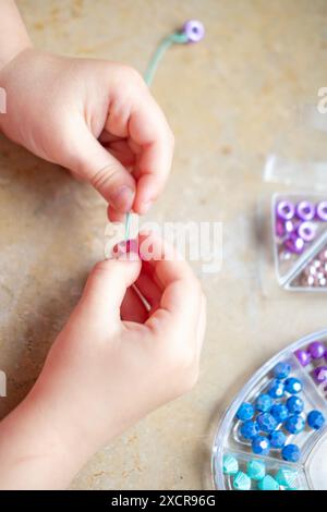 Fille d'âge préscolaire engagée dans l'activité d'art et d'artisanat, projet d'artisanat de bricolage, fabrication de bracelet personnalisé avec des perles colorées, motricité fine, promotion Banque D'Images