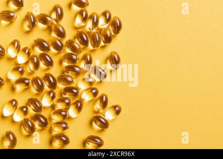 Capsules de vitamine D3 ou capsules d'huile de poisson oméga-3 sur fond jaune, vue de dessus, espace de copie. Gélules dorées à l'huile, supplément nutritionnel. Banque D'Images