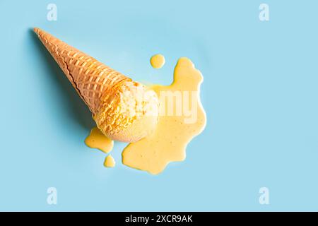 Crème glacée jaune fondant et renversant du cône de gaufre sur fond bleu pastel. Concept de cuisine estivale créative tendance et minimaliste. Pelle fondue Banque D'Images