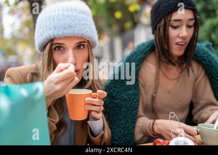 Deux femmes profitant d'une pause café à l'extérieur, habillées à la mode hivernale. Idéal pour le contenu sur la socialisation, les activités hivernales et les moments agréables. Banque D'Images