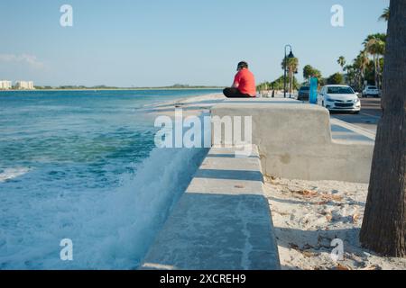 Vue moyenne de la station de levage en béton sur la droite avec l'eau qui s'écoule rapidement. Femme assise sur la chemise rouge droite. Près du coucher du soleil avec la lumière du soleil et l'ombre. Banque D'Images