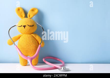 Lapin jouet avec stéthoscope sur fond de couleur, espace pour le texte Banque D'Images