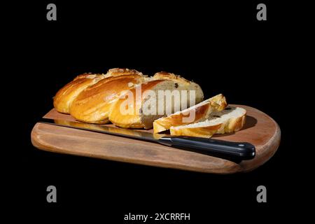 Un pain tressé fraîchement cuit, garni d'amandes et garni de raisins secs, est partiellement tranché et exposé sur une planche à découper en bois. La brea Banque D'Images