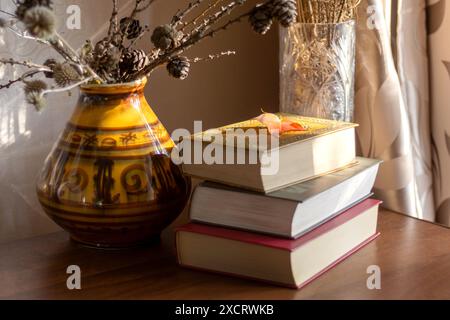 Nature morte avec des livres et des fleurs séchées dans un vase sur table dans une pièce éclairée par le soleil couchant Banque D'Images