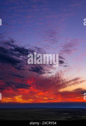 Portrait d'un ciel couchant avec le croissant de lune vieux de deux jours au milieu de nuages colorés au-dessus de la prairie. C'était de Writing-on-Stone provincial Banque D'Images