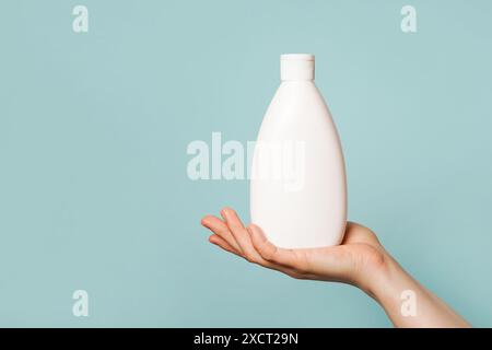 une main tenant une bouteille en plastique blanche sur un fond bleu clair Banque D'Images