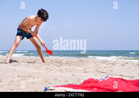 garçon pré-adolescent jouant sur la plage avec une pelle Banque D'Images