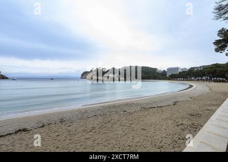 Une vue sereine sur la plage de Cala Galdana à Minorque, avec des eaux calmes et des falaises côtières. Le premier plan de la plage de sable mène à un cadre pittoresque de crique Banque D'Images