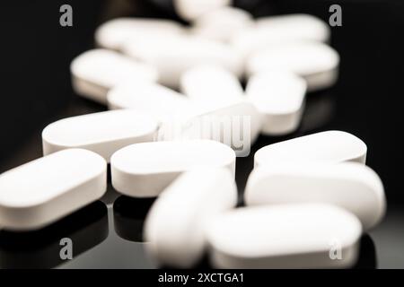 Un gros plan capture de nombreuses pilules ovales blanches étalées sur un fond sombre réfléchissant, mettant en évidence les inquiétudes concernant les opioïdes comme le fentanyl et Banque D'Images