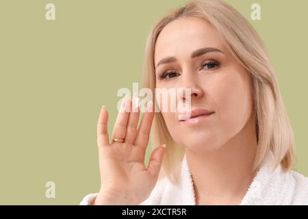 Belle femme mature en peignoir appliquant la crème sur fond vert Banque D'Images