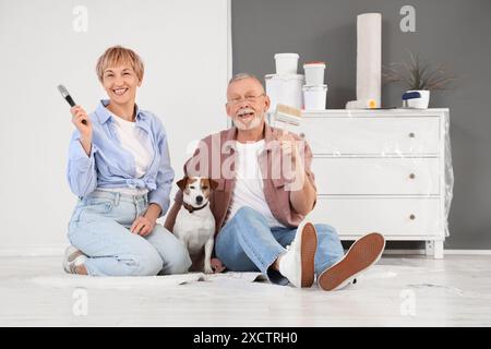 Couple mûr avec des pinceaux et chien assis sur le sol pendant la réparation dans leur nouvelle maison Banque D'Images