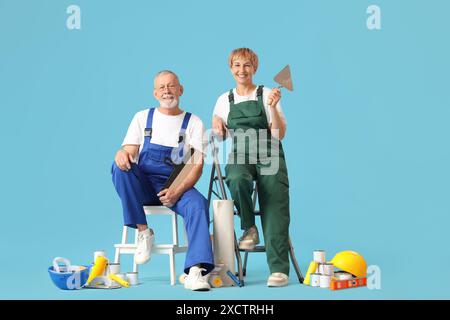 Couple mature de décorateurs avec des outils de peinture sur fond bleu Banque D'Images