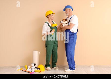 Couple mûr de décorateurs avec des outils de chien et de peinture près du mur beige Banque D'Images