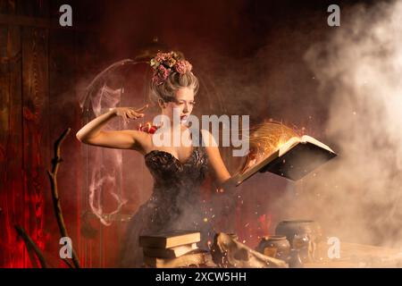 Jeune femme attrayante vêtue d'une robe noire vintage, tenant un livre de sorts dans le vieux château. Célébration d'Halloween, concept de sorcellerie, atmosphère mystique de conte de fées. Conjurant des sorts magiques. Banque D'Images