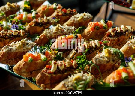 Une sélection exquise de bruschetta artisanale avec une variété de garnitures comprenant des fruits de mer, des légumes verts et des épices, présentée sur un élégant plateau en verre Banque D'Images