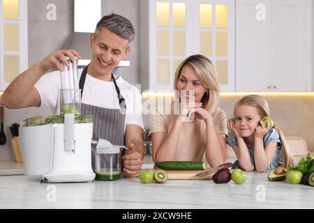 Famille heureuse avec presse-agrumes et produits frais faisant boisson à la table en marbre blanc dans la cuisine Banque D'Images
