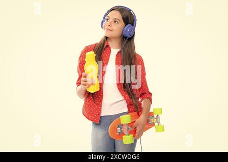 Jeune fille d'école avec bouteille d'eau de planche à roulettes et casque sur fond isolé de studio. Printemps écofille tendance, urbain style adolescent. Banque D'Images