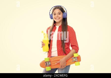 Jeune fille d'école avec bouteille d'eau de planche à roulettes et casque sur fond isolé de studio. Mode printemps écolière, style adolescent urbain. Portrait de Banque D'Images