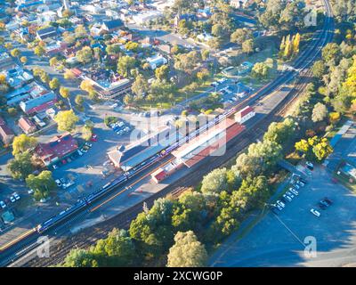 Vue aérienne des voies ferrées avec train en gare montrant les parkings, véhicules, bâtiments, routes et arbres, Castlemaine, Victoria, Australie. Banque D'Images