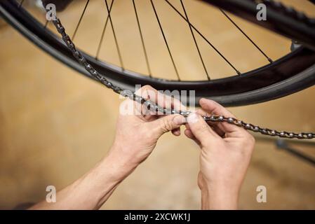 Réparateur travaillant : homme méconnaissable verrouillant la chaîne d'un vélo dans son atelier de vélo. De vraies personnes au travail. Vue rapprochée des mains. Banque D'Images