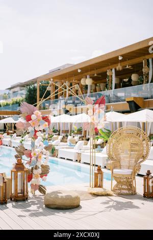 Arche de mariage colorée se tient près d'une chaise en osier près de la piscine avec chaises longues doubles sous parasols Banque D'Images