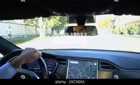 Yeux du conducteur masculin réfléchissant le rétroviseur pendant la conduite d'une voiture électrique. Homme confiant conduisant une voiture moderne en ville. Jeune homme regardant Banque D'Images