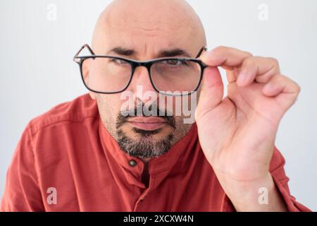 Un homme d'âge moyen ajustant ses lunettes tout en portant une chemise rouge, avec une expression concentrée Banque D'Images