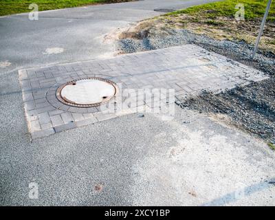 Puits nouvellement construit avec couvercle de trou d'homme sur une route asphaltée rurale en bavière. Banque D'Images