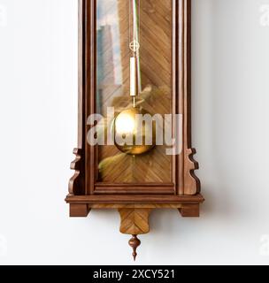 Une horloge de grand-père antique fixée au mur en bois avec des chiffres romains et une porte en verre sur un fond de surface blanche - rendu 3D. Banque D'Images