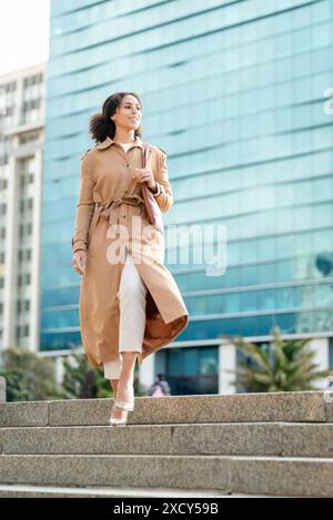 Entrepreneur de femme noire confiante marchant près de l'immeuble de bureaux moderne dans une tenue élégante Banque D'Images