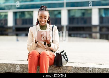 Femme d'affaires afro-américaine utilisant Tablet en plein air, souriant et travaillant à distance Banque D'Images