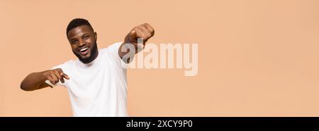 Joyeux jeune homme pointant et souriant sur fond beige Banque D'Images