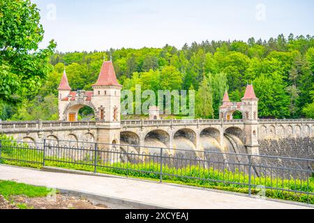 Une vue sur le barrage les Kralovstvi en Tchéquie, avec la structure emblématique en forme de château avec son pont voûté. Le barrage est entouré de verdure luxuriante et l'eau coule librement sur le déversoir. Banque D'Images