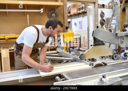 Friendly carpenter avec protège-oreilles et des vêtements de travail travaillant sur une scie dans l'atelier Banque D'Images