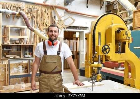 Portrait d'un carpenter en vêtements de travail et de protection de l'ouïe dans l'atelier d'un atelier du menuisier Banque D'Images
