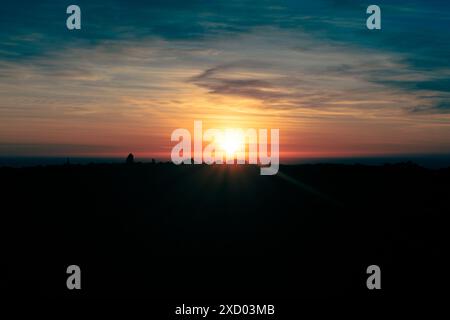 Superbe coucher de soleil sur l'horizon, projetant des couleurs vibrantes dans le ciel avec des rochers et des buissons silhouettes au premier plan. Banque D'Images